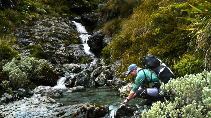 a-hiker-drinks-fresh-water-from-a-pure-mountain-stream-in-new-zealand_nylyupsr__F0000